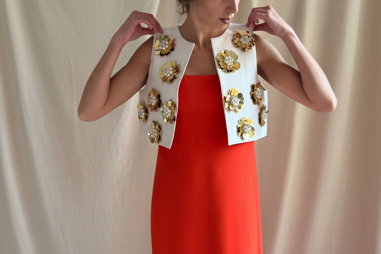 Woman wearing a red dress with a white embroidered jacket against a beige background